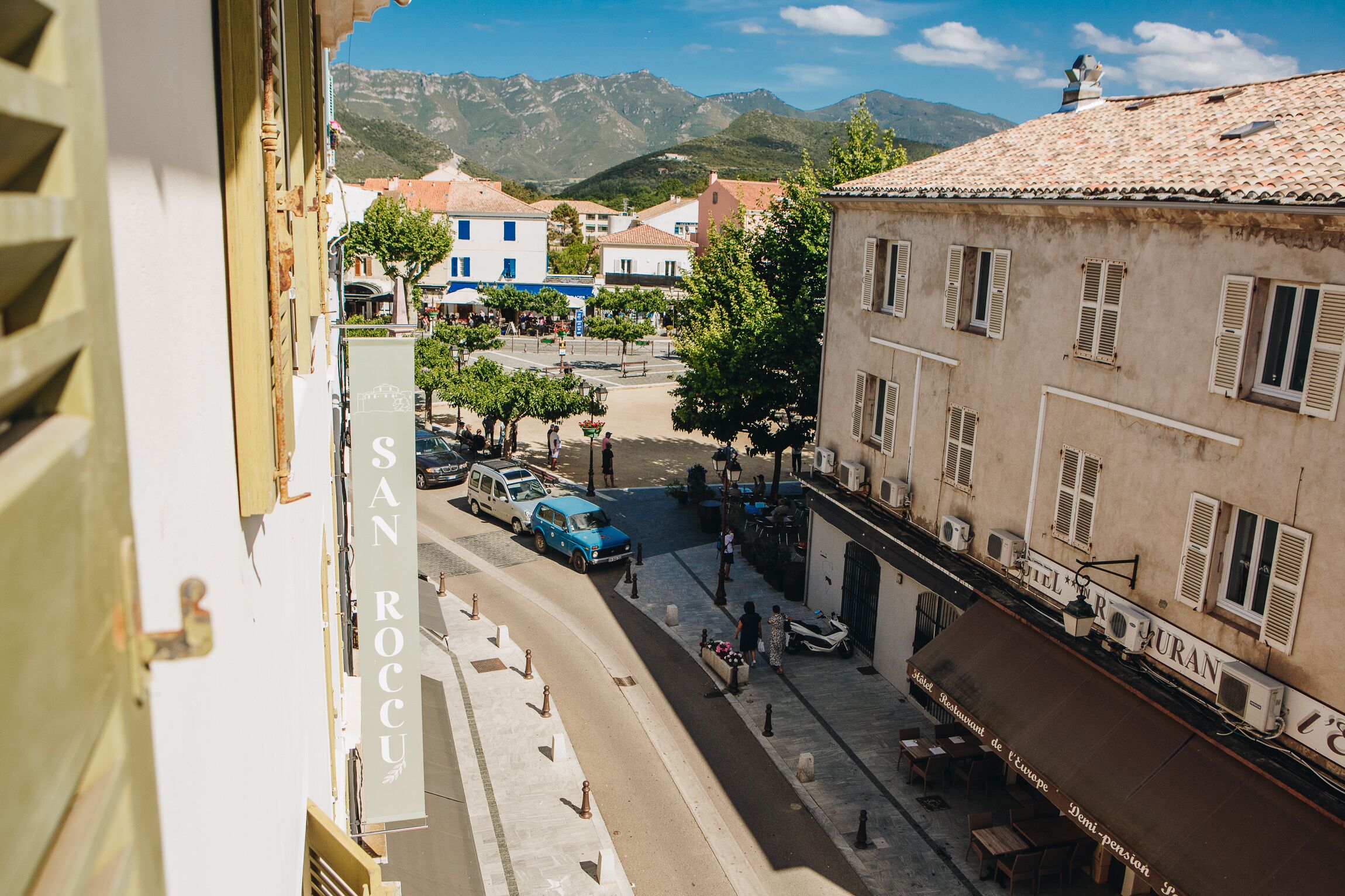 Vista de la calle con edificios, un restaurante llamado "Hotel Rurano" y un cartel que indica "San Rocco".