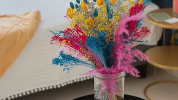 Una cama con sábanas blancas y un florero con flores coloridas sobre una mesita redonda.