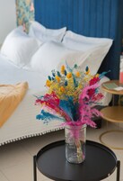 Un lit avec du linge de lit blanc et un vase rempli de fleurs colorées, posé sur une petite table ronde.