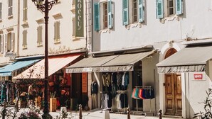 Vista de calle con un edificio que dice "SANROCCU" y una tienda llamada "TAMARELLA" con exhibiciones de ropa para exteriores.