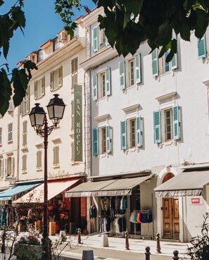 Une vue de rue avec un bâtiment portant l’inscription « SANROCCU » et une boutique nommée « TAMARELLA », où sont exposés des vêtements d’extérieur.