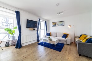 A modern living room with a white sofa, a grey sofa, a coffee table, and a TV mounted on the wall. - Homely 2-bed Apartment in London (London)
