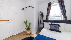 A bedroom with a bed, a bedside shelf, a potted plant, and a window with curtains. - Homely 2-bed Apartment in London (London)