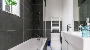 A modern bathroom with a bathtub, toilet, and sink. - Homely 2-bed Apartment in London (London)