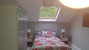 Ein Schlafzimmer mit Oberlicht, einem Bett mit floralem Bettzeug, zwei Nachttischen mit Lampen und einem Kleiderschrank.