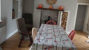 Ein Esszimmer mit einem langen Tisch, Stühlen, einer Uhr, einem Kamin und einer hängenden Leuchte.