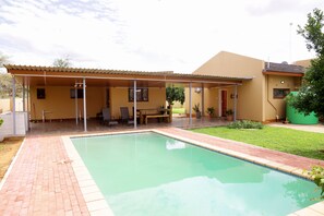 A covered outdoor area with a pool, a patio, and a house in the background. - HAITHOMS TLOKWENG (Gaborone)