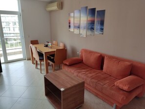 A living room with a wooden coffee table, a red sofa, a dining table with chairs, and a balcony view.