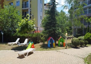 A courtyard with lounge chairs, a children's play area, and a building in the background.