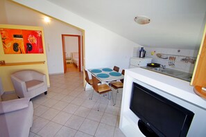 Ein Essbereich mit Tisch und Stühlen, einer Couch, einem Fernseher und einer Küche inklusive Spüle und Geschirr.