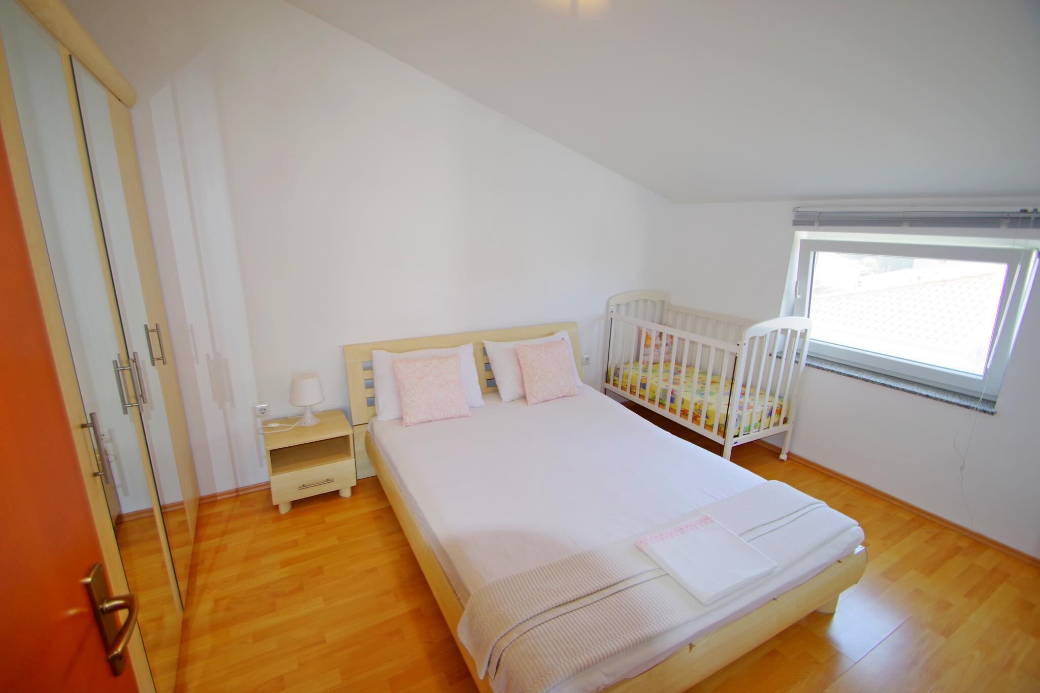 A bedroom with a bed, a crib, a nightstand, and a window.