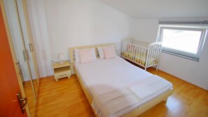 Ein Schlafzimmer mit einem Bett, einem Babybett, einem Nachttisch und einem Fenster.