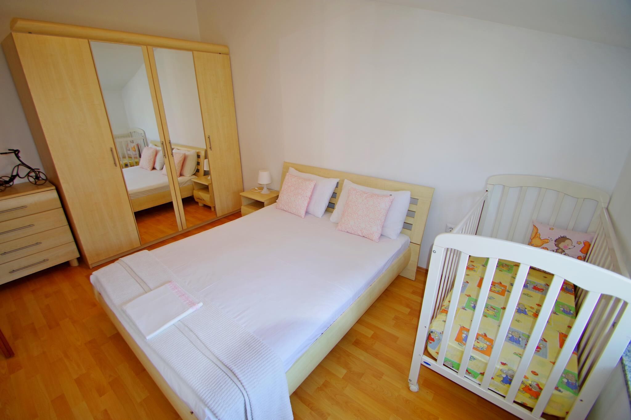 A bedroom with a large wardrobe, a single bed, a crib, and a bedside table with a lamp.