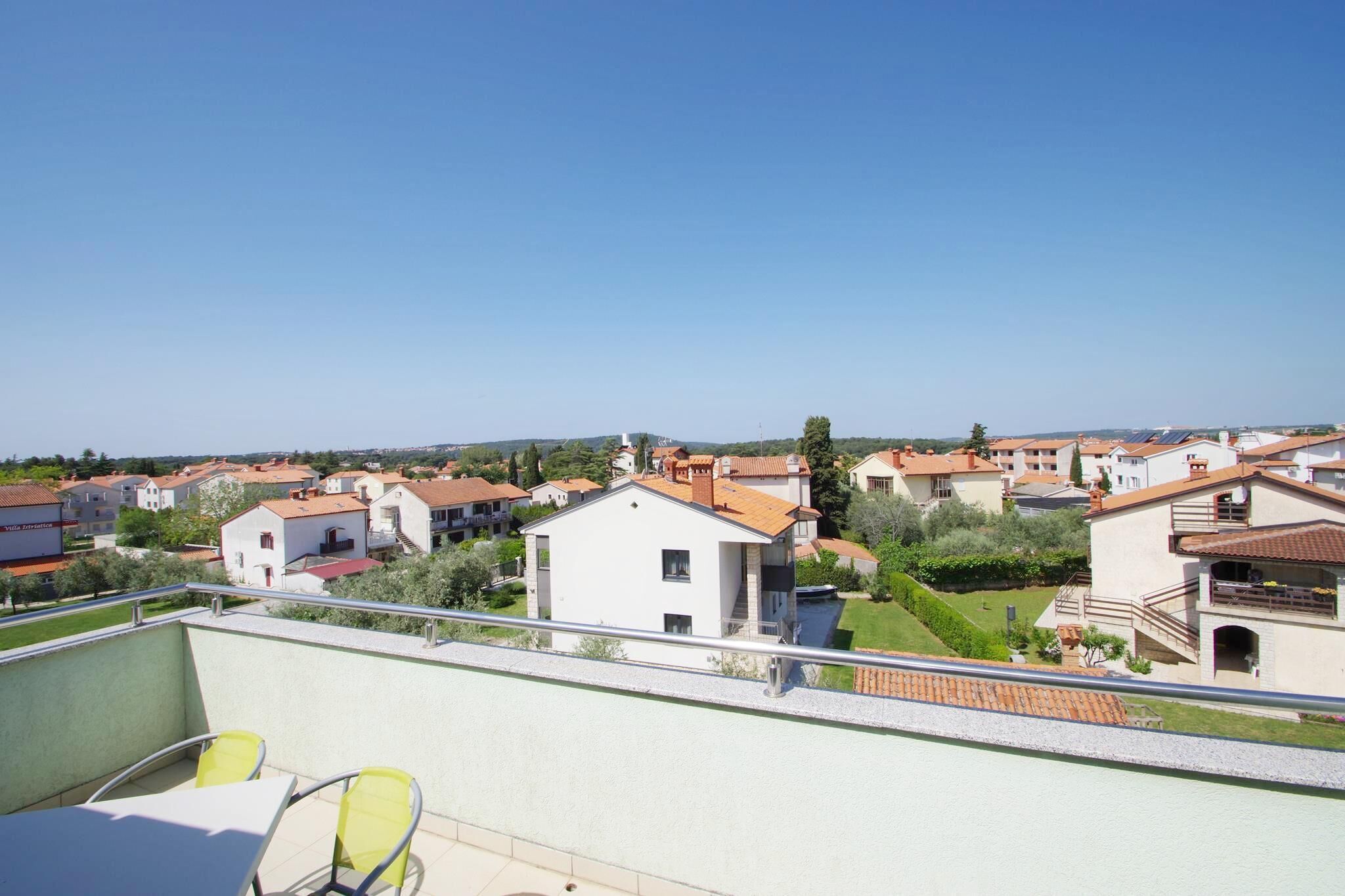 Et boligområde med huse, en balkon med gule stole, og en klar blå himmel.
