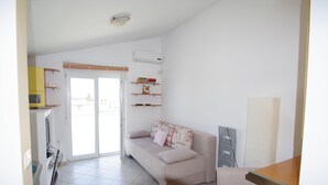 Ein Wohnzimmer mit einer Couch, einem Esstisch und einer Küchenzeile inklusive Schränken und Mikrowelle.