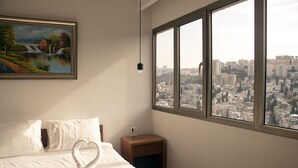 Habitación de hotel con cama, un cuadro, una mesita de noche y un ventanal con vistas a la ciudad.