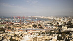 Un paisaje urbano costero con una zona portuaria, incluyendo grúas y contenedores de envío.