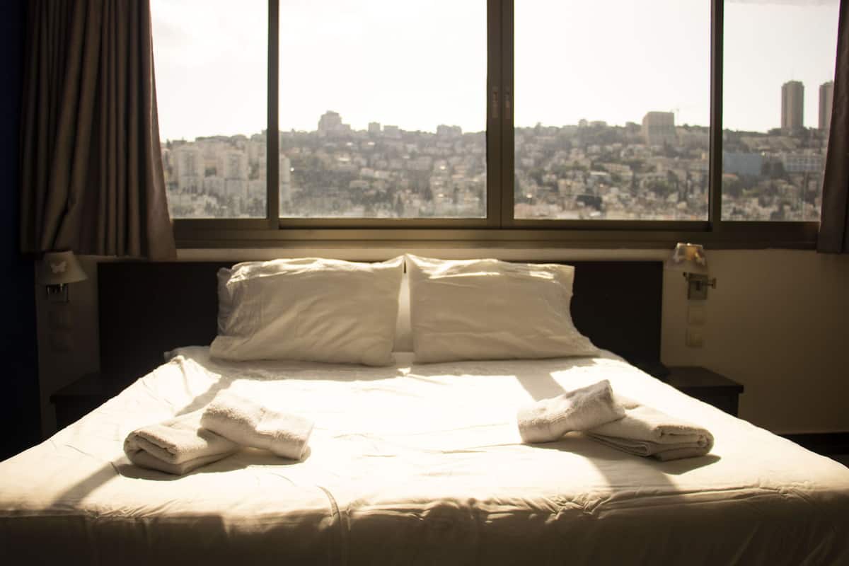 A hotel room with a large bed, two pillows, and two folded towels.