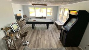 A pool table in a room with a sofa, a television, and a gaming console.