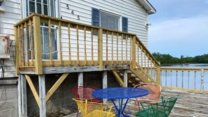 A wooden deck with a blue table and colorful chairs, overlooking a body of water.