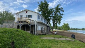 A two-story building with a balcony and a red star on the roof, located near a body of water.