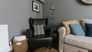 A living room with a black leather armchair, a beige sofa, a floor lamp, and a woven basket. - DUNDAS COTTAGE - 3 Bed in Richmond North Yorkshire (Richmond)