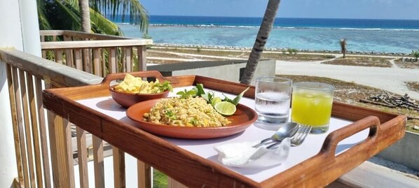 A tray with food and drinks on a balcony overlooking the ocean.