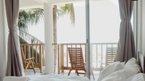Een slaapkamer met een bed, een houten stoel en een balkon met uitzicht op palmbomen.