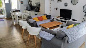 Uma sala de estar moderna com um sofá cinzento, cadeiras brancas, uma mesa de centro de madeira e uma televisão.