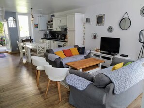 Een moderne woonkamer met een grijze bank, witte stoelen, een houten salontafel en een televisie.
