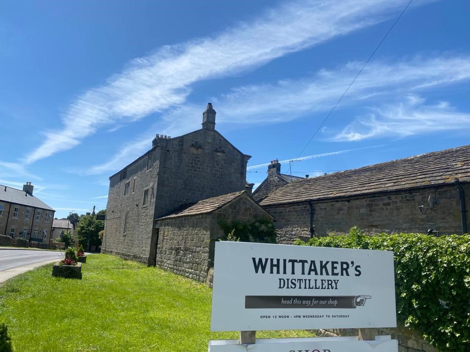 A sign for Whittaker's Distillery with a stone building in the background.