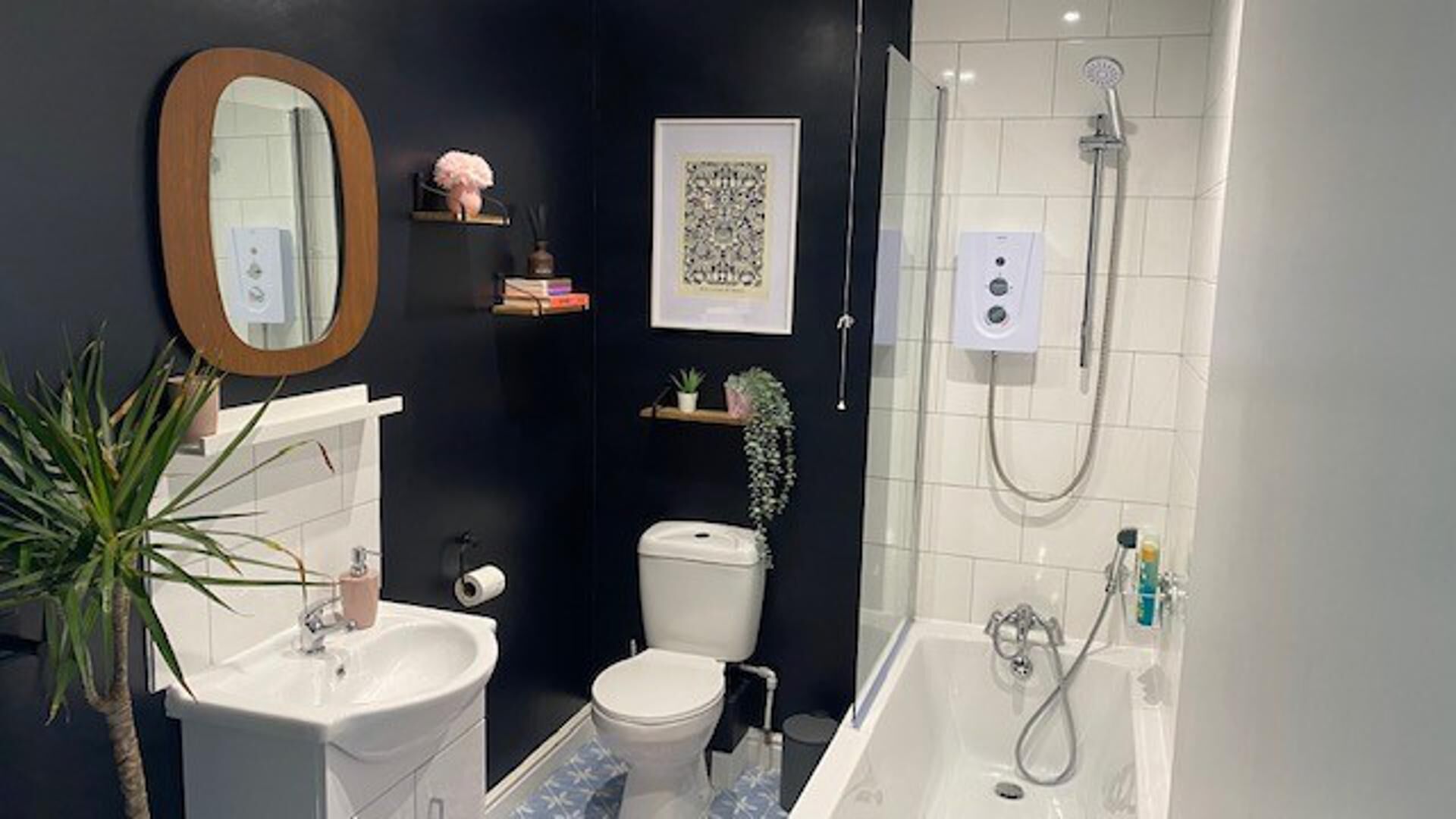 Um banheiro moderno com pia, vaso sanitário e banheira. Há um espelho, um quadro emoldurado e uma pequena prateleira com objetos decorativos.