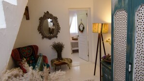 A hallway with a mirror, a lamp, a chair, and a decorative wall panel. - Aracati Pansiyon (Cesme)