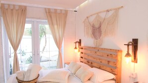 A bedroom with a wooden bed, white bedding, a bedside table with a lamp, and a view through a window with curtains. - Aracati Pansiyon (Cesme)