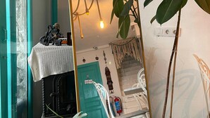 A room with a teal door, a white chair, a potted plant, a large mirror, and a hanging light fixture. - Aracati Pansiyon (Cesme)