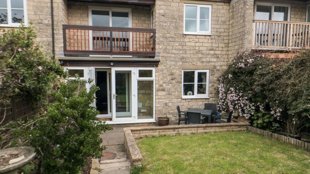 Un bâtiment en pierre à deux étages, doté d’un balcon, d’une terrasse avec des meubles d’extérieur et d’une pelouse bien entretenue.