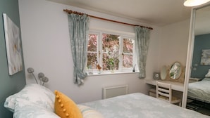 Une chambre à coucher avec un lit, une commode, une fenêtre avec des rideaux et un radiateur.