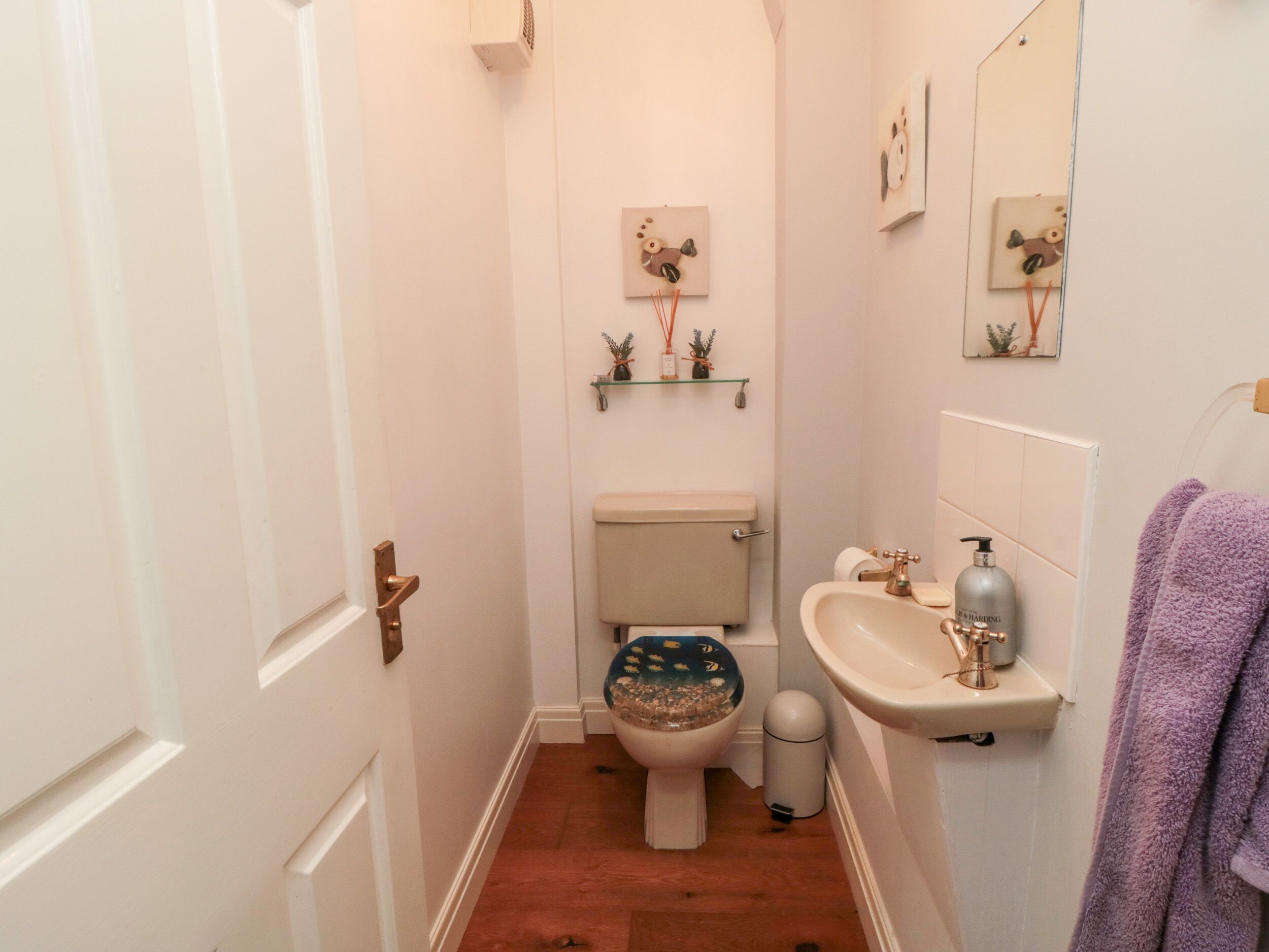 A small bathroom with a toilet, sink, and a mirror. There are decorative items on the wall and a towel hanging on the right.