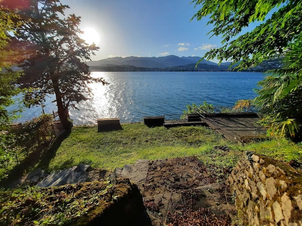 Blick auf einen See mit einer Holzterrasse, einer Steinmauer und üppiger Vegetation.