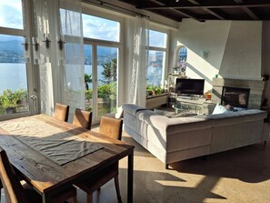 A living room with a sofa, a TV, and a fireplace. There is a dining table with chairs. - Vacation home with an exclusive view of the lake, on Lake Lugano—lakefront property, hiking area. (Lugano)