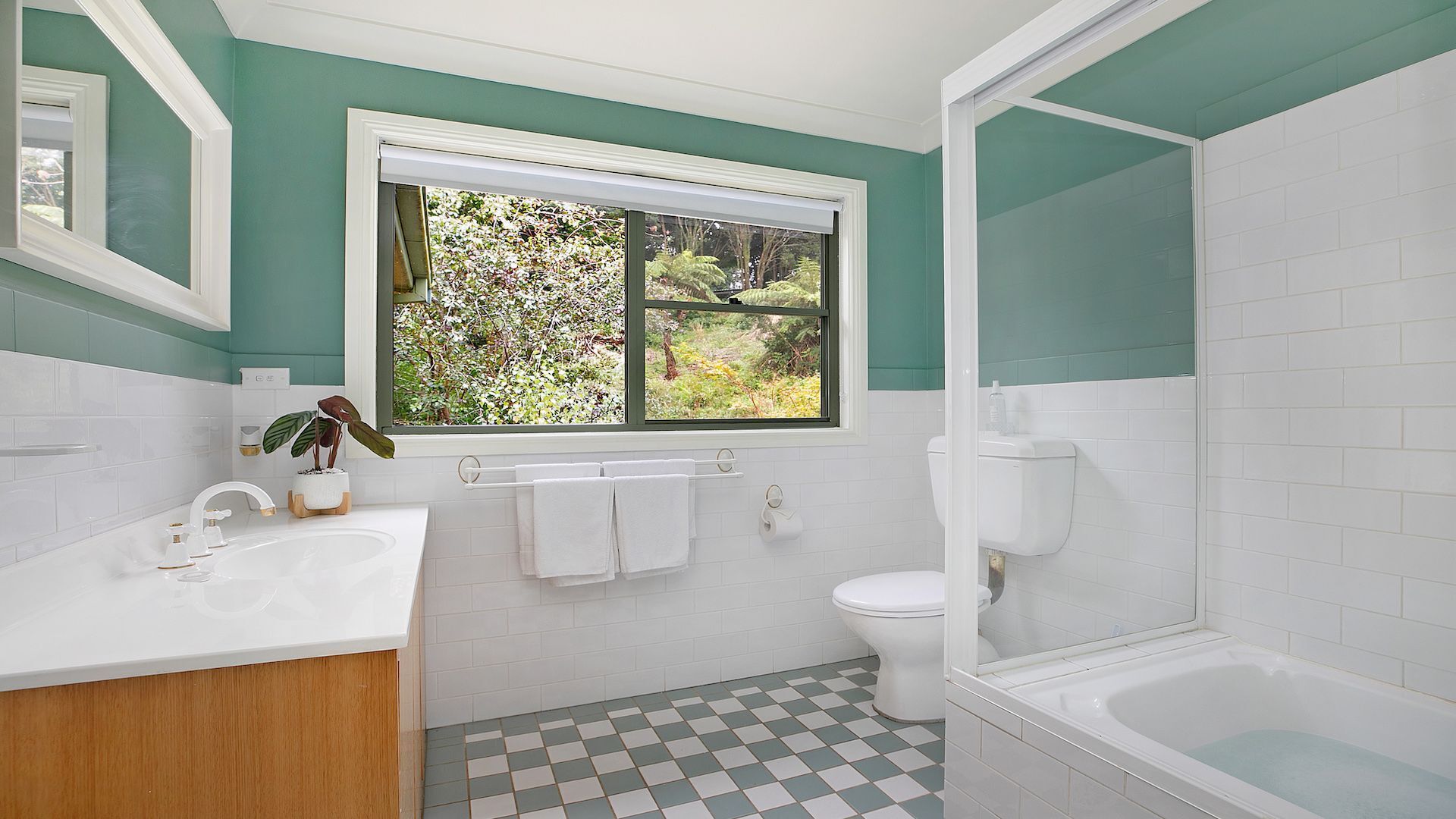 A bathroom with a white sink, a toilet, a bathtub, and a window with a view of greenery.