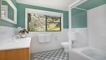 A bathroom with a white sink, a toilet, a bathtub, and a window with a view of greenery.