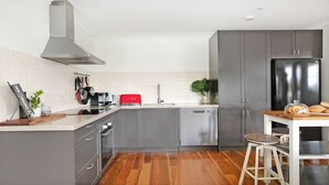 Una cocina moderna con armarios grises, una campana extractora de acero inoxidable, un tostador rojo y una mesa de comedor de madera con taburetes.
