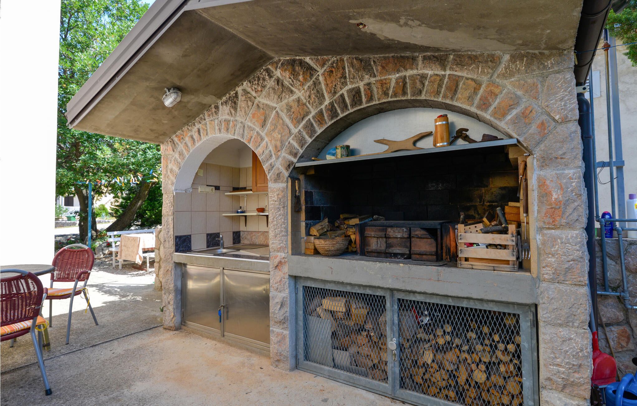Une cuisine extérieure dotée d’arches en pierre, d’un évier encastré et d’un espace aménagé autour d’un foyer.