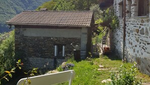 Ein Steinhaus mit Ziegeldach, einem kleinen Fenster und einer hölzernen Bank im Vordergrund.