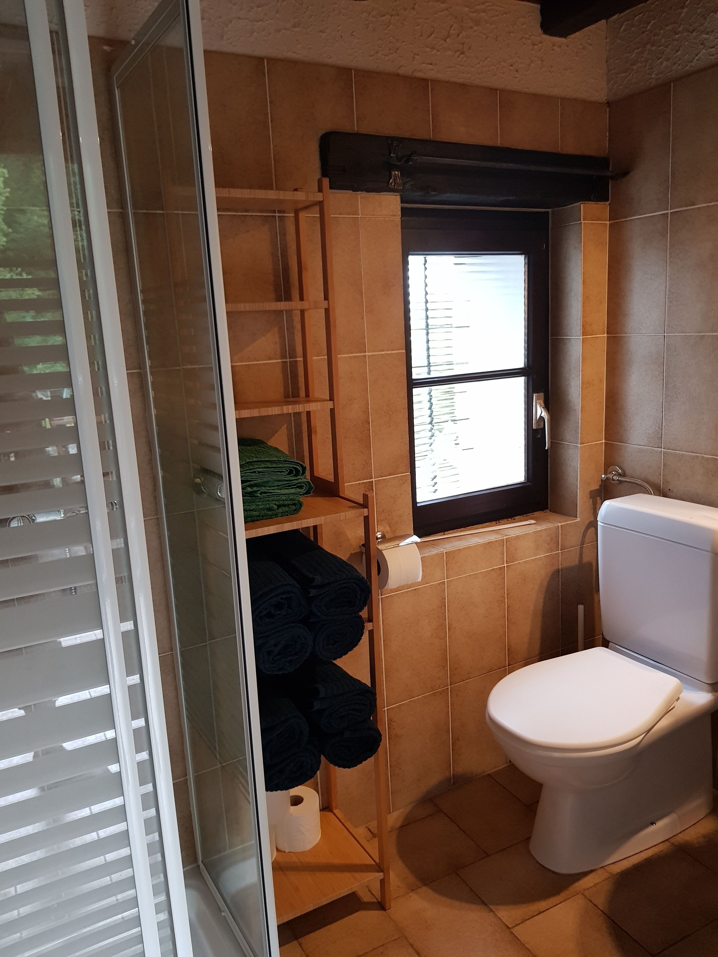 Et badeværelse med toilet, et vindue og hylder med håndklæder.