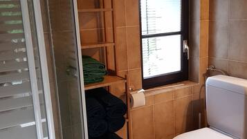 Et badeværelse med toilet, et vindue og hylder med håndklæder.