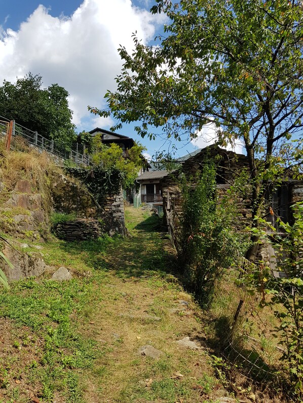 A stone building with a stone pathway leading to it, surrounded by greenery and a clear sky.