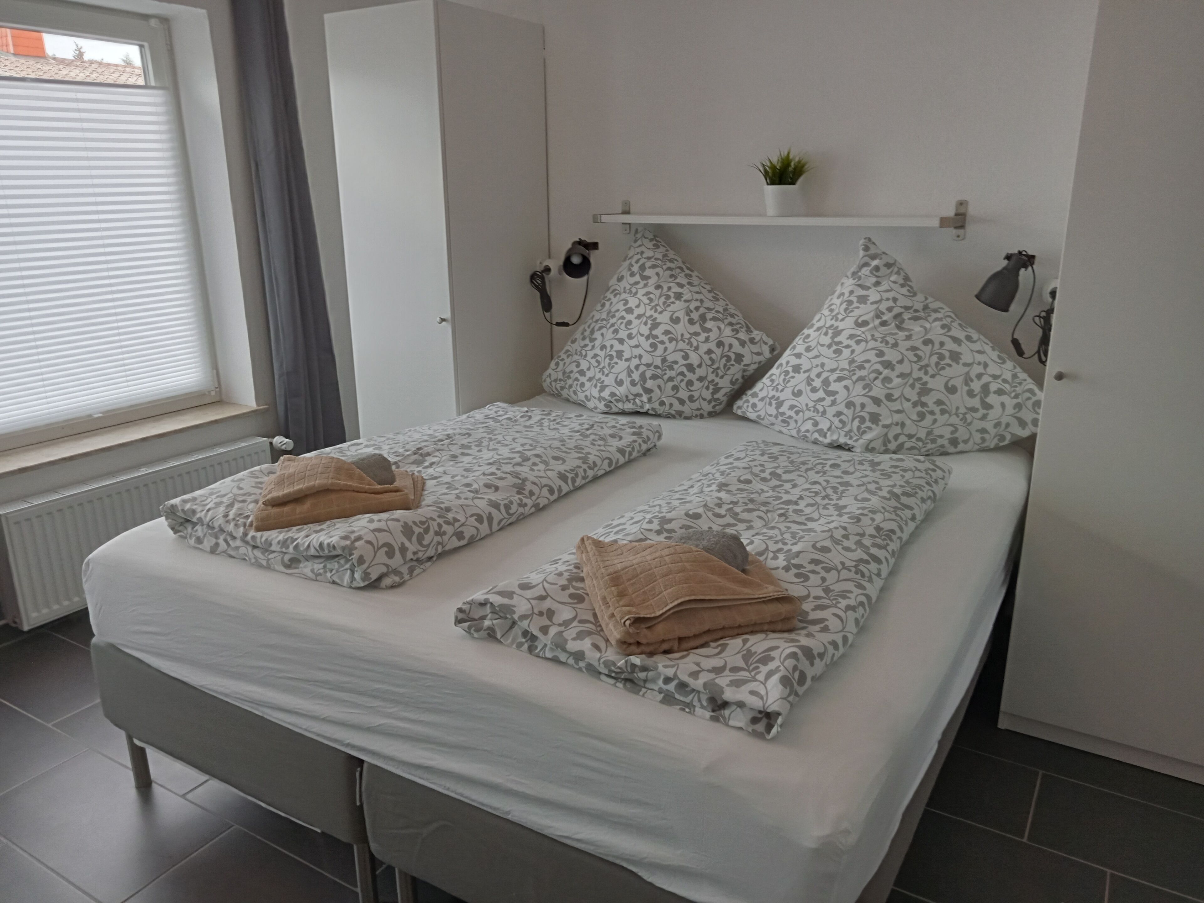 A double bed with patterned bedding, a small shelf with a plant, and a radiator.