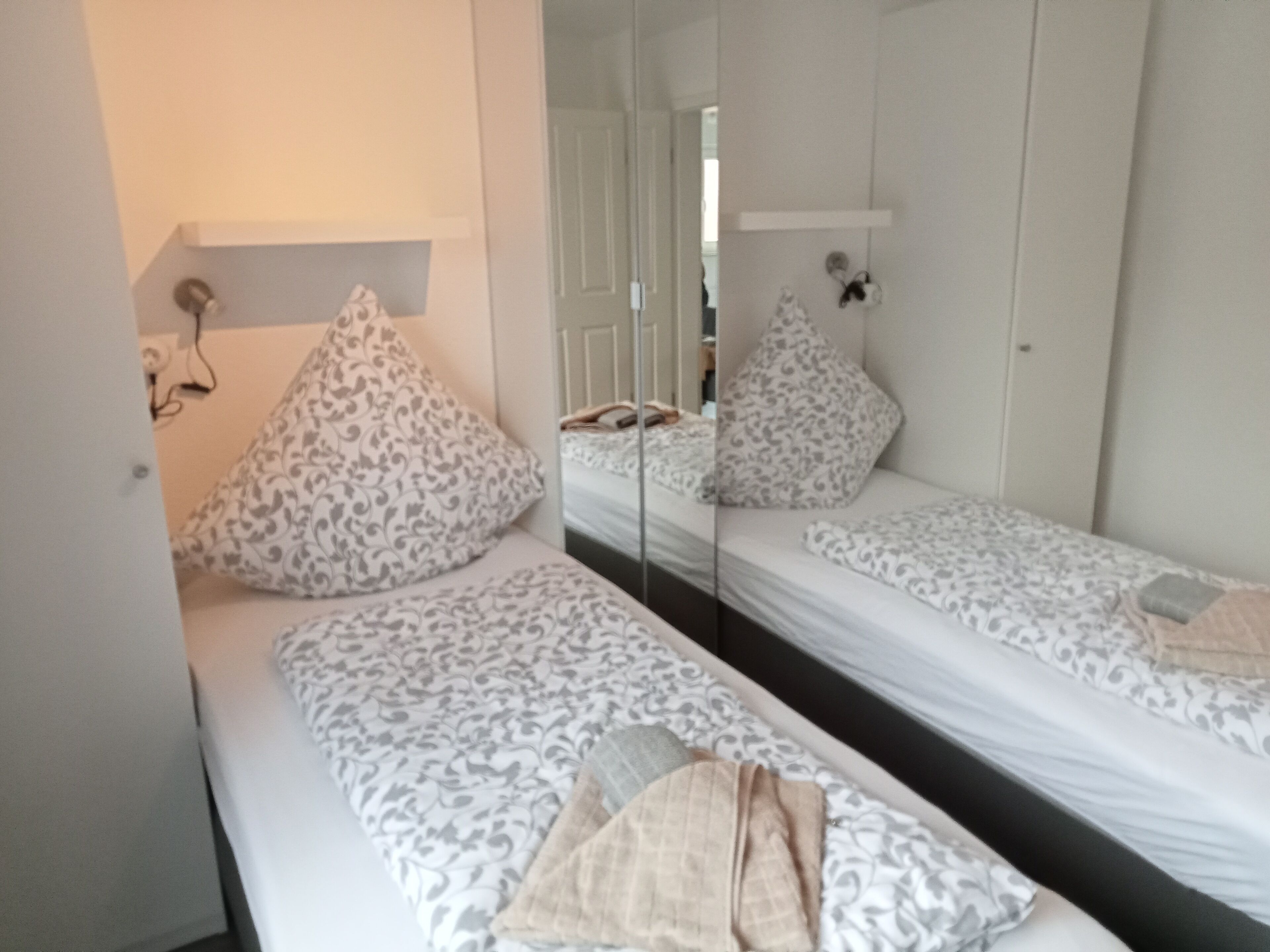 A bedroom with a single bed, a mirror, and a wardrobe.